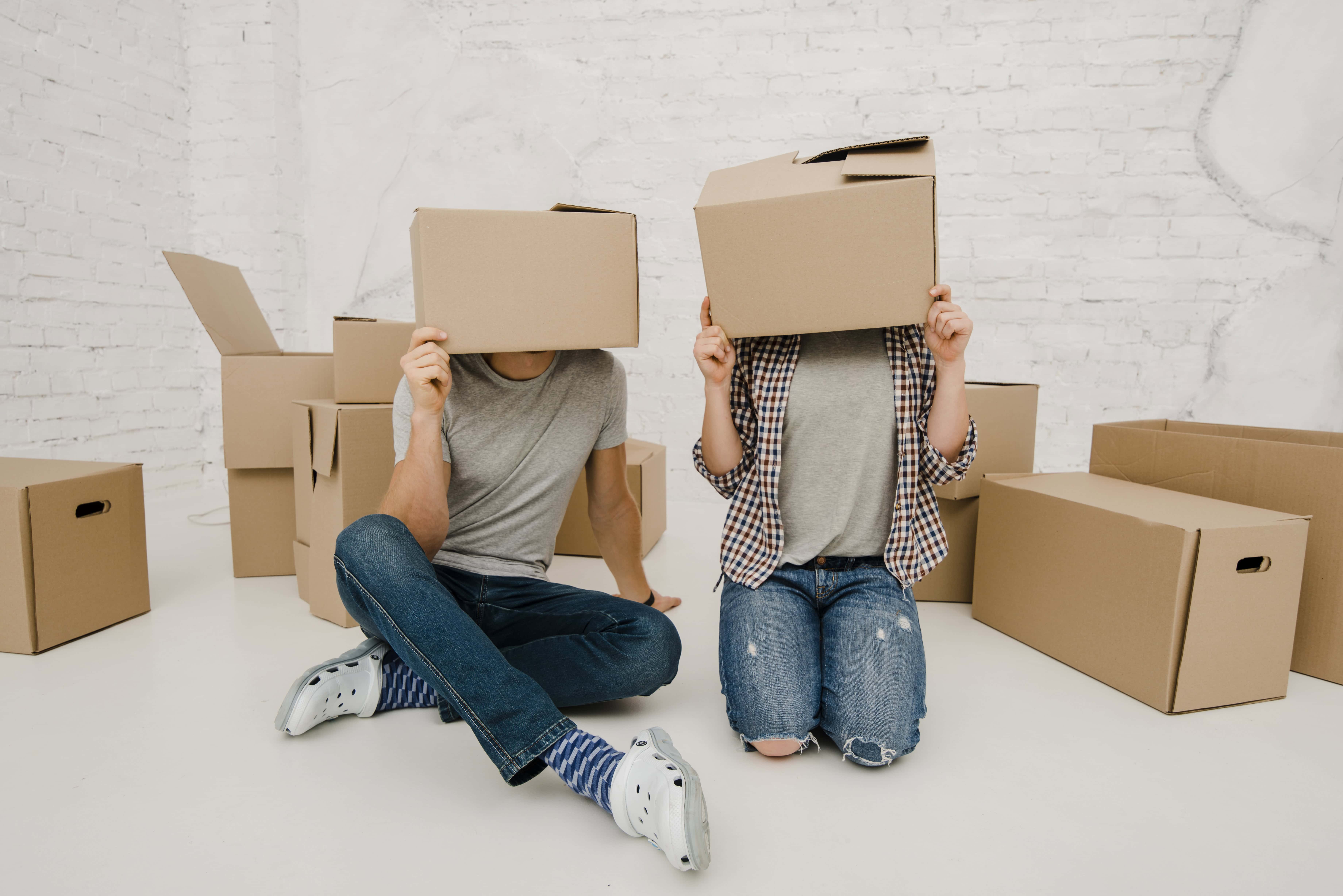 Kids with moving boxes over their heads, packing for a move or relocation, in a modern room with cardboard boxes.