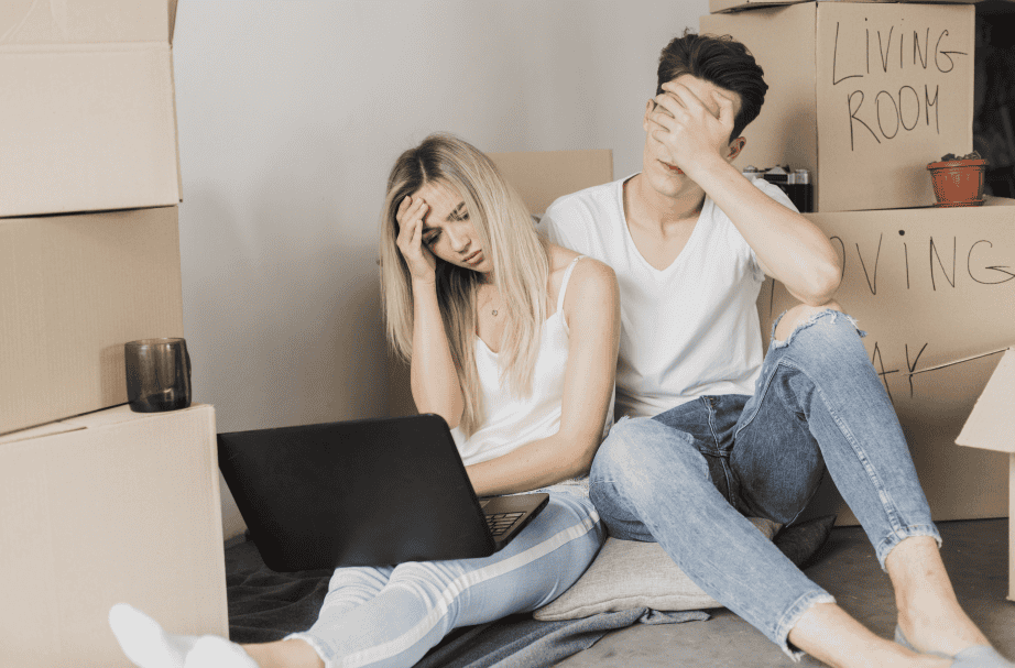 Overwhelmed young couple during move-in stress, surrounded by boxes and packing supplies.